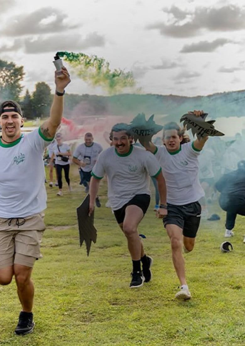 lfac_camp-counselors-running-to-the-front_mobile lfac excited camp counselors running across field with colorful smoke and team flags during camp rally