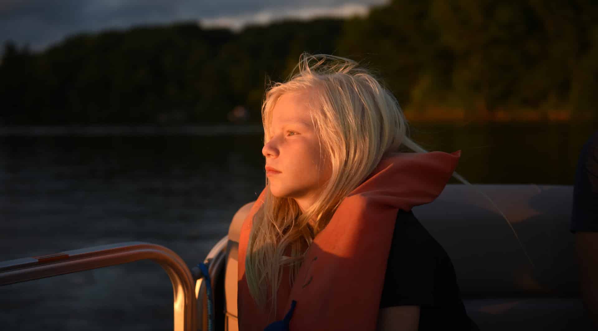 lfac young camper wearing life jacket peacefully watching sunset from boat on calm lake