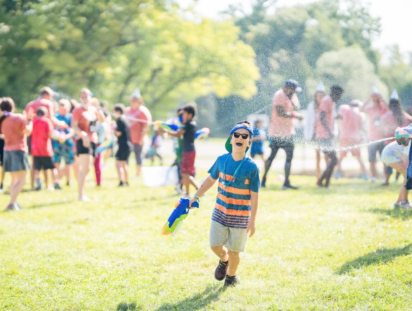 lfac happy child wearing sunglasses laughing and playing with water gun during outdoor camp event